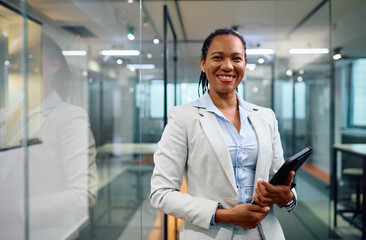 Happy black female CEO with touchpad in office looking at camera.