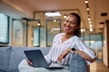 Happy black businesswoman using laptop in office and looking at camera.