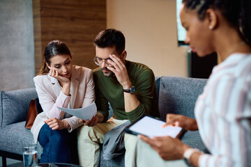 Worried couple going through financial reports during meeting with insurance agent.