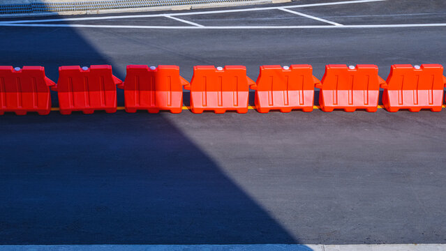 Row of orange plastic barriers on the middle of asphalt road in outdoor car parking with sunlight and shadow on surface