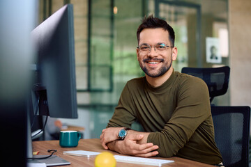Happy male entrepreneur at his office desk looking at camera.