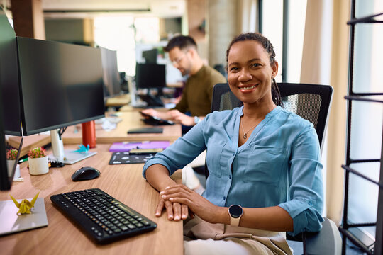 Happy African American businesswoman at her office desk looking at camera.