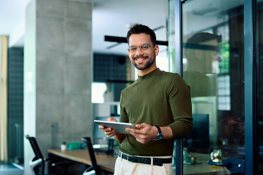 Happy entrepreneur using digital tablet in office and looking at camera.