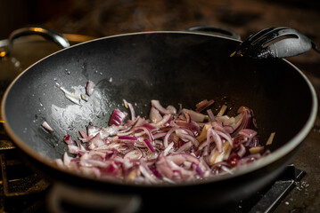 Fry the onion in a deep frying pan. Purple chopped onion is being prepared for cooking.