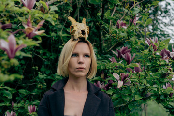 Sensual erotic woman with an animal skull on her head against the backdrop of blooming magnolia.
