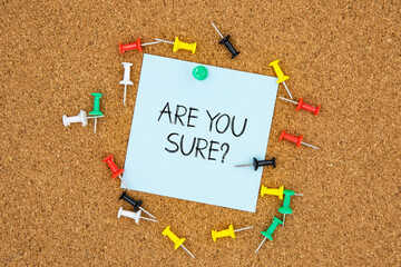 Are you sure question text on light blue post-it paper pinned on bulletin cork board surrounding by multi color pins. This message can be used in business concept about asking are you sure.