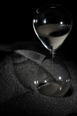 Hourglass stand on black sand with silhouette shadow over black background. Black hourglass show more time Deadline extended time management hope concept hour glass, life clock passing by