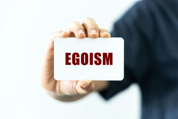 Egoism text on blank business card being held by a woman's hand with blurred background. Business concept about egoism.