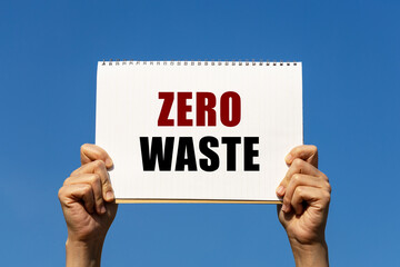 Zero waste text on notebook paper held by 2 hands with isolated blue sky background. This message can be used as business concept about zero waste.