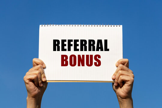 Referral bonus text on notebook paper held by 2 hands with isolated blue sky background. This message can be used as business concept about referral bonus.