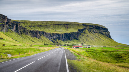 Icelandic landscape around farmland, waterfall from the cliff in the distance, Iceland.