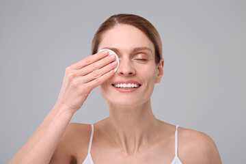 Beautiful woman removing makeup with cotton pad on gray background