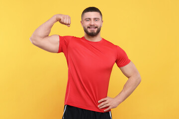 Fototapeta na wymiar Portrait of handsome man showing muscles on yellow background