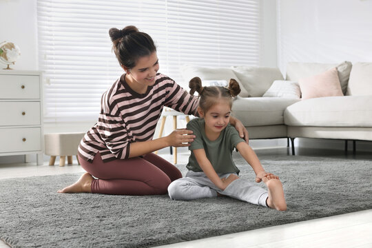 Young mother and her daughter stretching together at home