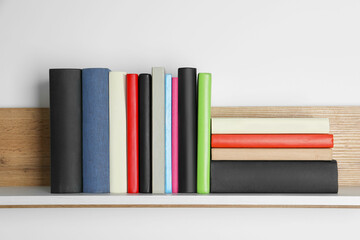 Different books on wooden shelf near white wall
