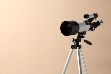 Tripod with modern telescope on beige background, closeup. Space for text