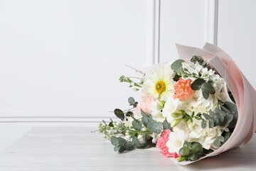 Bouquet of beautiful flowers on wooden table near white wall. Space for text
