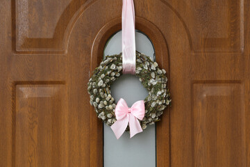 Wreath made of beautiful willow branches and pink bow on wooden door