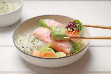Delicious spring rolls wrapped in rice paper on white wooden table, closeup