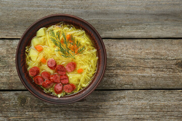 Bowl of delicious sauerkraut soup with smoked sausages and dill on old wooden table, top view. Space for text