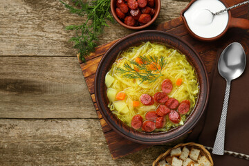 Delicious sauerkraut soup with smoked sausages and dill served on old wooden table, flat lay. Space for text