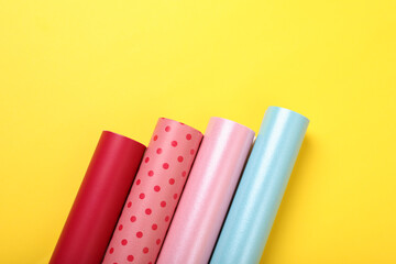 Rolls of colorful wrapping papers on yellow background, flat lay. Space for text