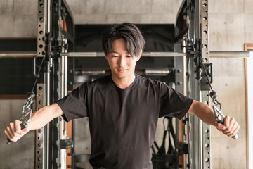 スポーツジムでケーブルマシンを使って筋トレをするアジア人男性
