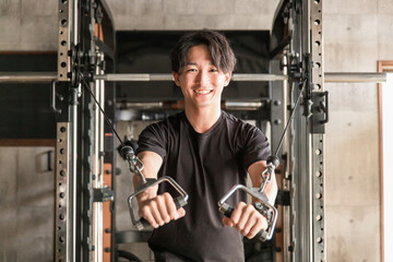 スポーツジムでケーブルマシンを使って筋トレをするアジア人男性

