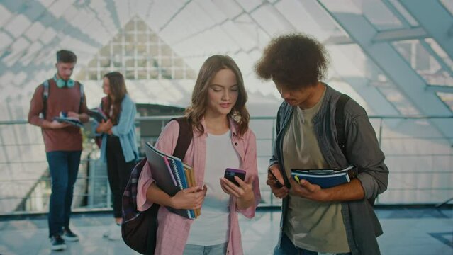Two Attractive Students Talking and Using Smartphone in the College Hallway. Digital Education. Future Technologie. Teamwork