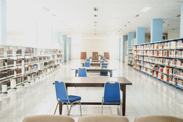 An empty college library with open spaces, blue chairs and book stacks. A modern light and airy building.