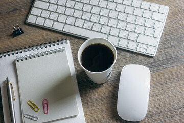 Notebooks, paper clips with a pen and coffee, on a wooden table with a keyboard and mouse