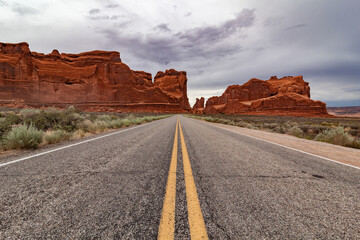 Highway to the world of arches. The red mountains in the background, bushes on the roadside, to go to an enchanted world. Arches National Park is a national park in eastern Utah in the United States. 