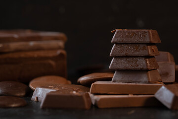 Stack of chocolate cubes and dark chocolate bars on black background. Dessert food background.