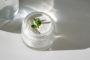 An open jar of facial scrub powder with a green sprig.