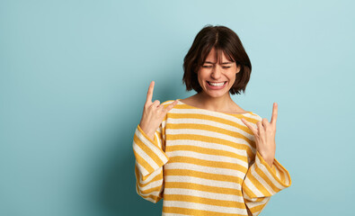 Joyful ethnic lady showing horns sign and smiling in blue studio
