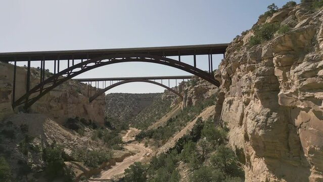 Aerial-Flying over desert dirt road passing under twin bridges of Interstate-70 over Eagle Canyon deep in the San Rafael Swell, a rugged feature of this geologic anticline formation.