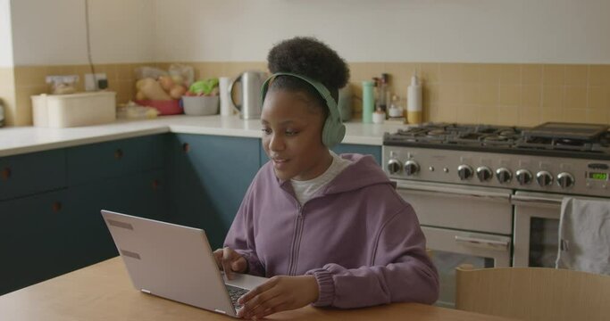 Female Teenager Studying Homework on Laptop in Kitchen