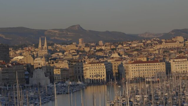 Cityscape of classic french port town architecture, harbor, and mountains behind at golden hour, static dutch angle