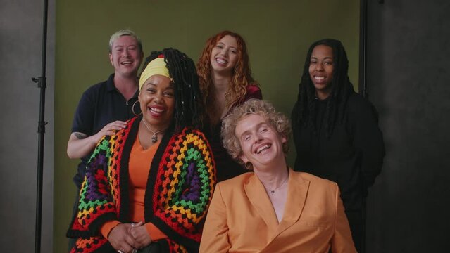 Five LGBTQIA queer people smiling and laughing against studio backdrop