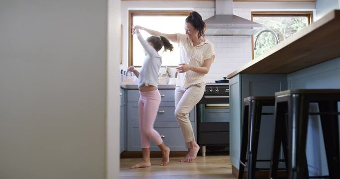 Dancing, girl and mother are free in the morning with energy at family house by holding hands. Child, mom and music in the kitchen with laughter in a home with fun dancer and bonding with humor.