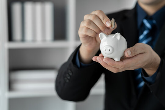 Cropped image of businessman standing holding piggy bank and putting coins into it The concept of saving money, investing, financial planning. cost savings.