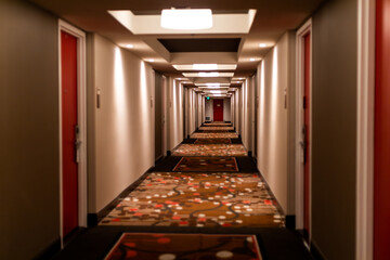 A hallway with a carpeted hallway that has a red and black rug that says hotel on it.