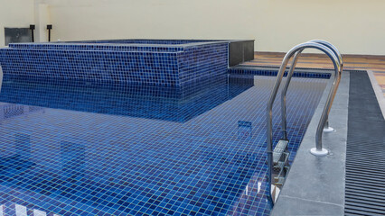 The blue tiled bottom is visible through the clear water. A staircase with metal handrails descends...