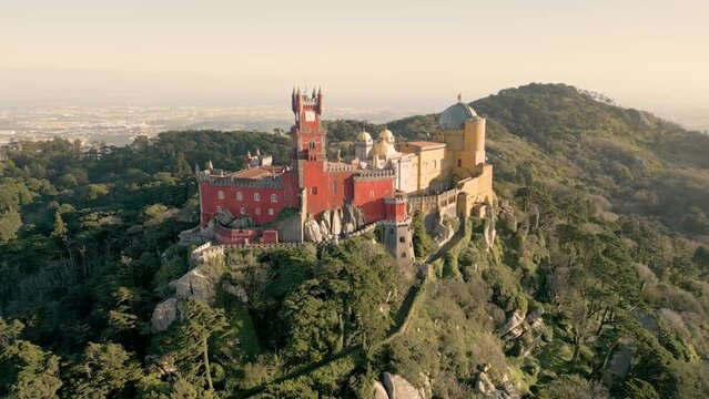 Slow aerial revealing shot of the stunning Pena Palace ontop of the mountains in Sintra