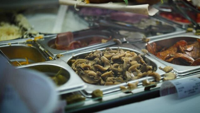 Cook Take Mushrooms On Tray Using Tongs On Food Showcase. - close up