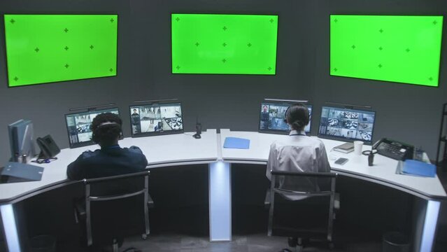 Multi ethnic male and female officers control CCTV cameras. Employees work in security control center. Computer monitors showing surveillance cameras video footage. Big digital screens with chromakey.