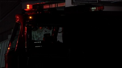 Red lights flash on the roof, above the cab of a firetruck in the USA at the scene of an emergency at night.