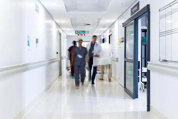 Blurred motion of diverse doctors and medical staff in busy hospital corridor, copy space