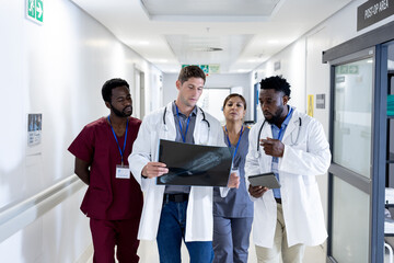 Diverse group of doctors discussing x ray walking in hospital corridor