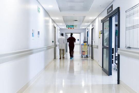 Blurred motion of diverse doctors walking in busy hospital corridor, copy space